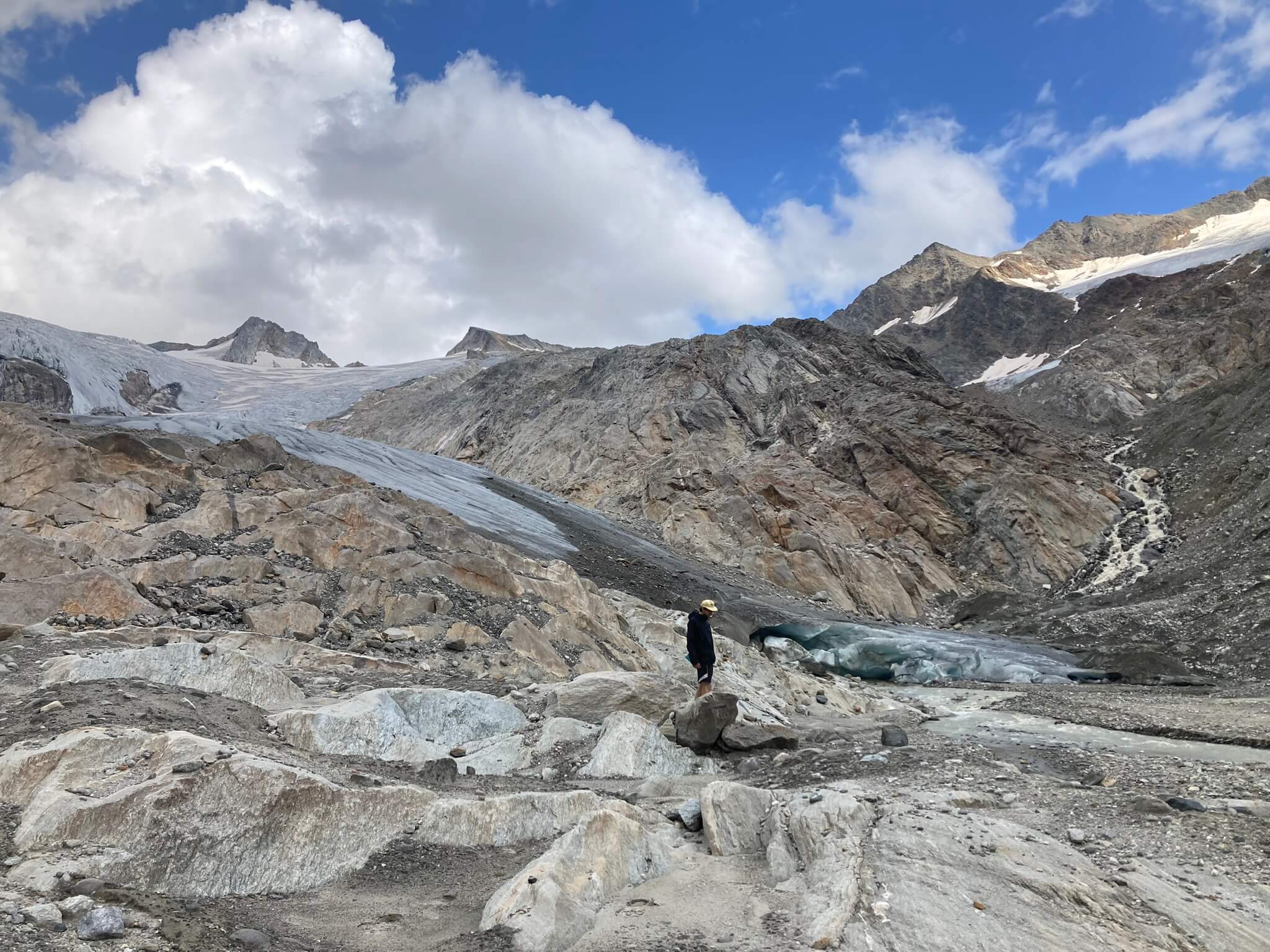 Ein Mann steht am Fuße des Gletschers. Die Bergwelt rund herum ist frei von Eis.