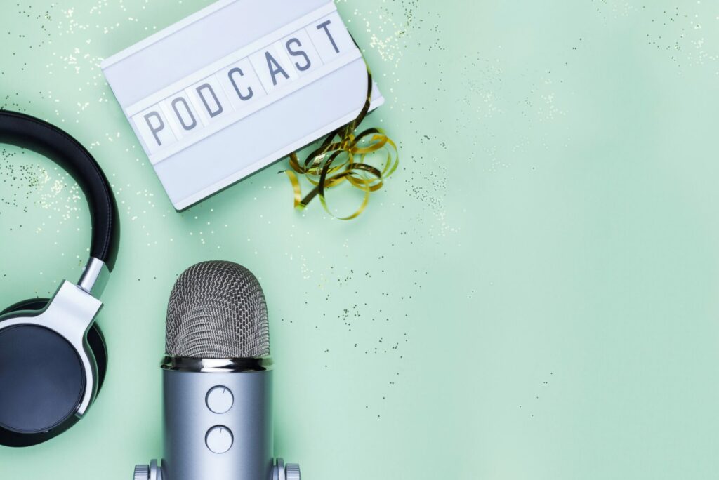 Bild zeigt Kopfhörer, ein Mikrofon und eine Kassette mit der Aufschrift "Podcast".